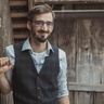 Portrait photograph of Dr Philipp Preinstorfer, a man with brown hair, a beard and glasses leaning against a timber building.  